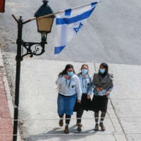 Schoolgirls walk underneath an Israeli flag in the city of Hebron in the occupied West Bank on Feb. 21. | AFP-JIJI