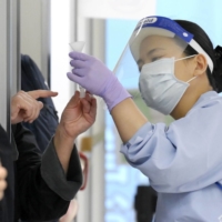 A quarantine officer checks a saliva sample from an overseas passenger who arrived at Narita International Airport in December. | KYODO

