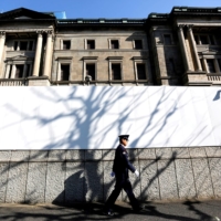 A security guard walks in front of the Bank of Japan headquarters in Tokyo. A surge in BOJ shares has confused market participants, as its stock pays a tiny dividend and holds no voting rights. | REUTERS 