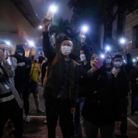 Supporters hold up their phones with the light on outside a court in Hong Kong on Friday after four pro-democracy activists charged for \"conspiracy to commit subversion\" were released on bail. | AFP-JIJI