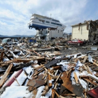 A ship washed ashore by the March 2011 tsunami rests on a two-story building in Otsuchi, Iwate Prefecture in April that year. | AFP-JIJI
