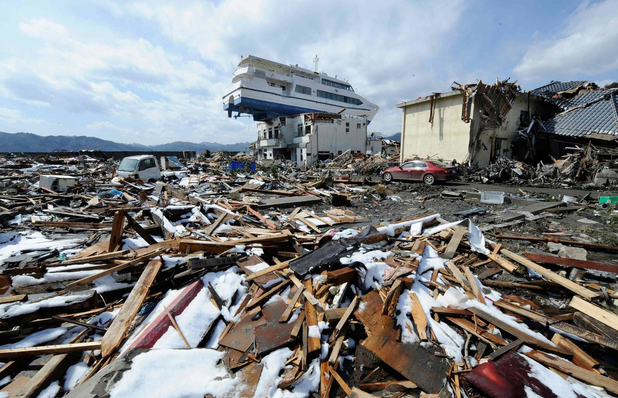 A ship washed ashore by the March 2011 tsunami rests on a two-story building in Otsuchi, Iwate Prefecture in April that year. | AFP-JIJI