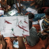 A Rohingya boy at the Balukhali refugee camp near Cox\'s Bazaar, Bangladesh, holds up a drawing about his experiences while fleeing Myanmar. | SERGEY PONOMAREV / THE NEW YORK TIMES
