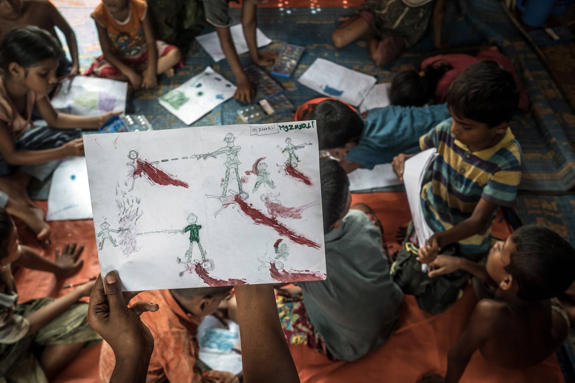A Rohingya boy at the Balukhali refugee camp near Cox's Bazaar, Bangladesh, holds up a drawing about his experiences while fleeing Myanmar. | Sergey Ponomarev / The New York Times