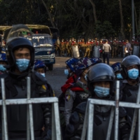Police and military forces stand by on Feb. 9 in Yangon, Myanmar, as tens of thousands of people gather on University Avenue Road to protest against the military\'s seizure of power. | THE NEW YORK TIMES