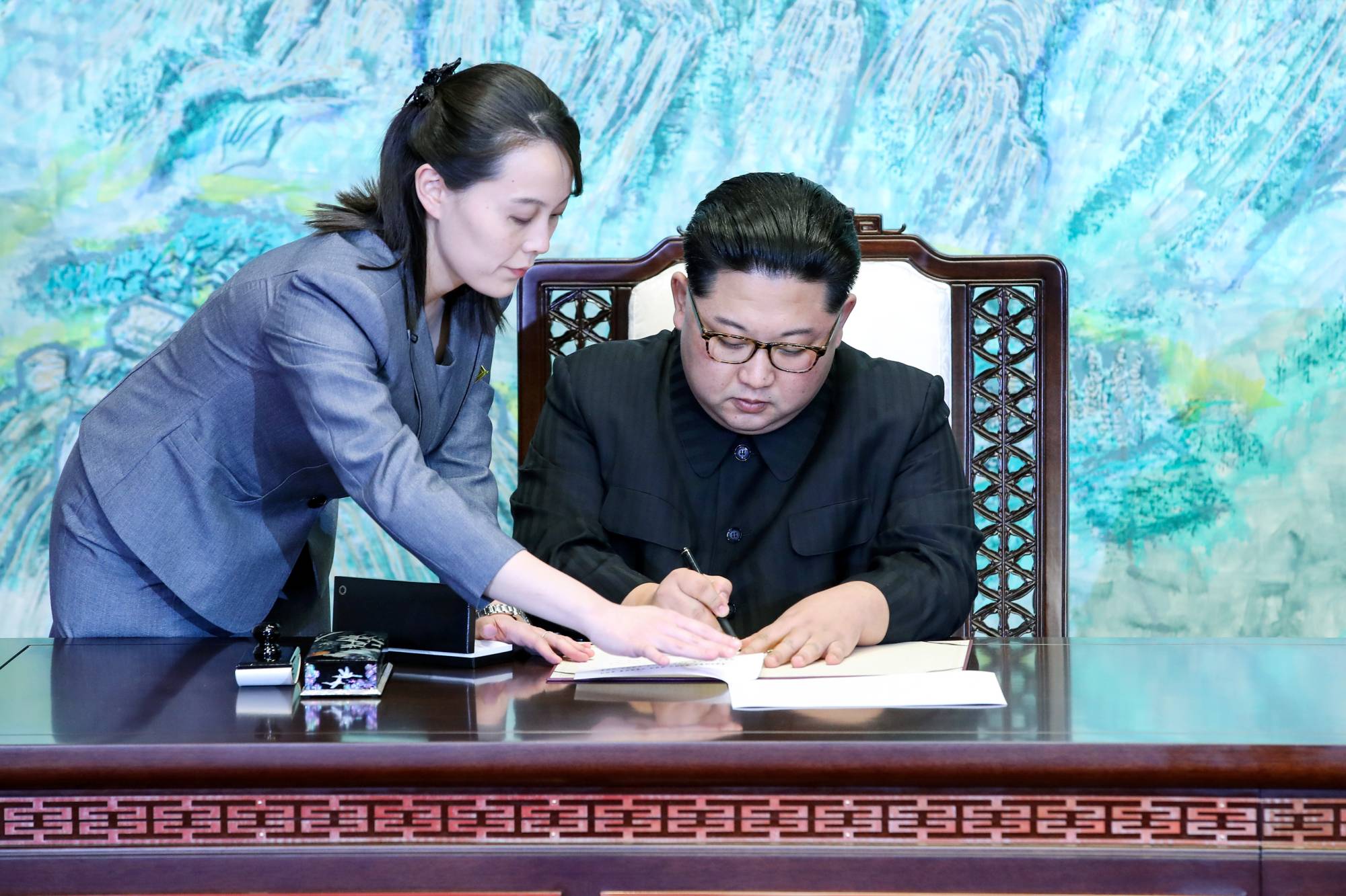 North Korean leader Kim Jong Un is assisted by his sister, Kim Yo Jong, as he signs documents at the truce village of Panmunjom in South Korea, inside the Demilitarized Zone separating the two Koreas, in April 2018.    | KOREA SUMMIT PRESS POOL / VIA REUTERS