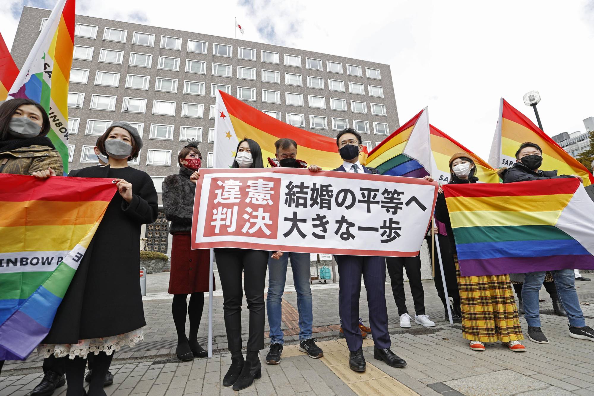 Lawyers and supporters of plaintiffs hold signs and flags outside the Sapporo District Court on Wednesday hailing a court decision that said Japan's failure to recognize same-sex marriage is unconstitutional. The sign says that the ruling is a 'big step forward for marriage equality.'  | KYODO