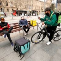 Delivery riders with backpacks of Glovo, Uber Eats and Deliveroo wait for orders in Barcelona on Feb. 26. | REUTERS