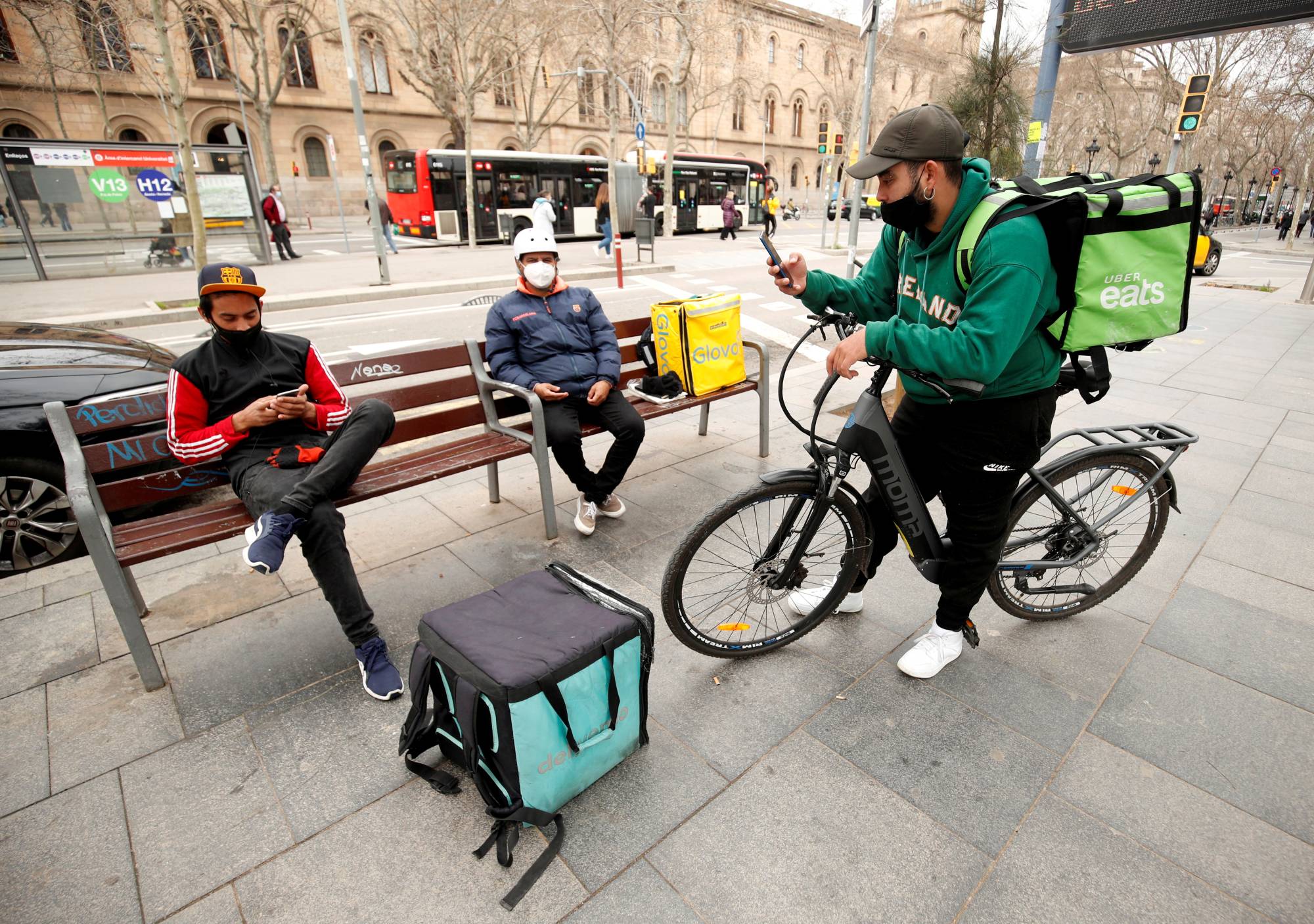 Delivery riders with backpacks of Glovo, Uber Eats and Deliveroo wait for orders in Barcelona on Feb. 26. | REUTERS