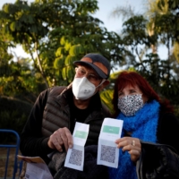 A couple pose for a photo with their \"green passport,\" a pass for those vaccinated against COVID-19 or those with presumed immunity, before entering a live performance venue in Tel Aviv in February. | REUTERS