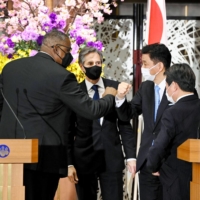 U.S. Defense Secretary Lloyd Austin (left) and Defense Minister Nobuo Kishi (second from right) do elbow bumps following a joint news conference in Tokyo on Tuesday. | POOL / VIA KYODO