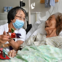 Mihoko Hoshihara, a 62-year-old nurse, presents a traditional doll made of origami paper to a patient undergoing palliative care at Minami Seikyo Hospital in Nagoya. | CHUNICHI SHIMBUN
