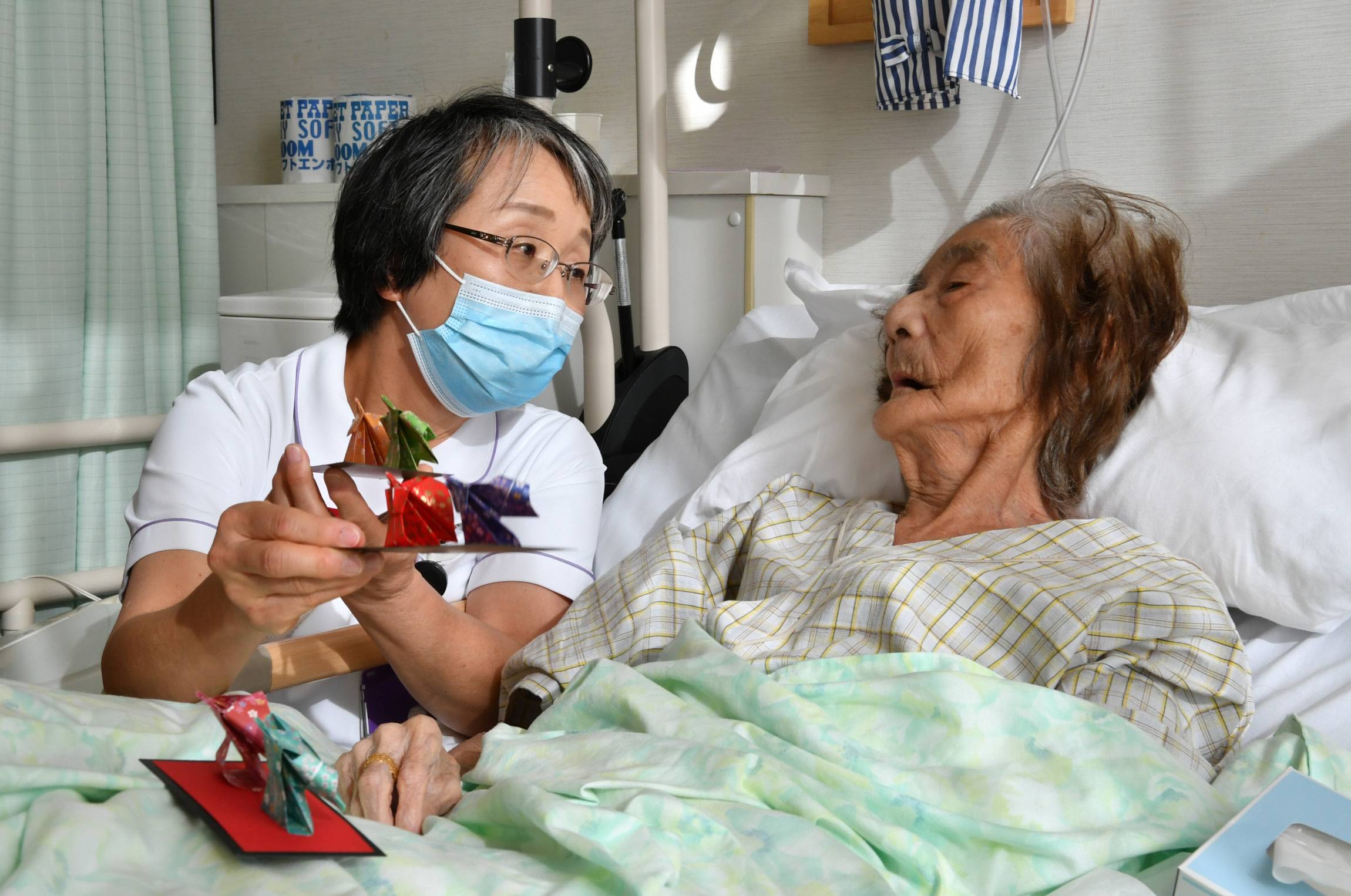 Mihoko Hoshihara, a 62-year-old nurse, presents a traditional doll made of origami paper to a patient undergoing palliative care at Minami Seikyo Hospital in Nagoya. | CHUNICHI SHIMBUN