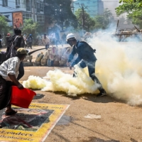 A man stands on a poster featuring armed forces chief Gen. Min Aung Hlaing as he attempts to douse tear gas during a crackdown by security forces in Yangon on Friday.  | AFP-JIJI