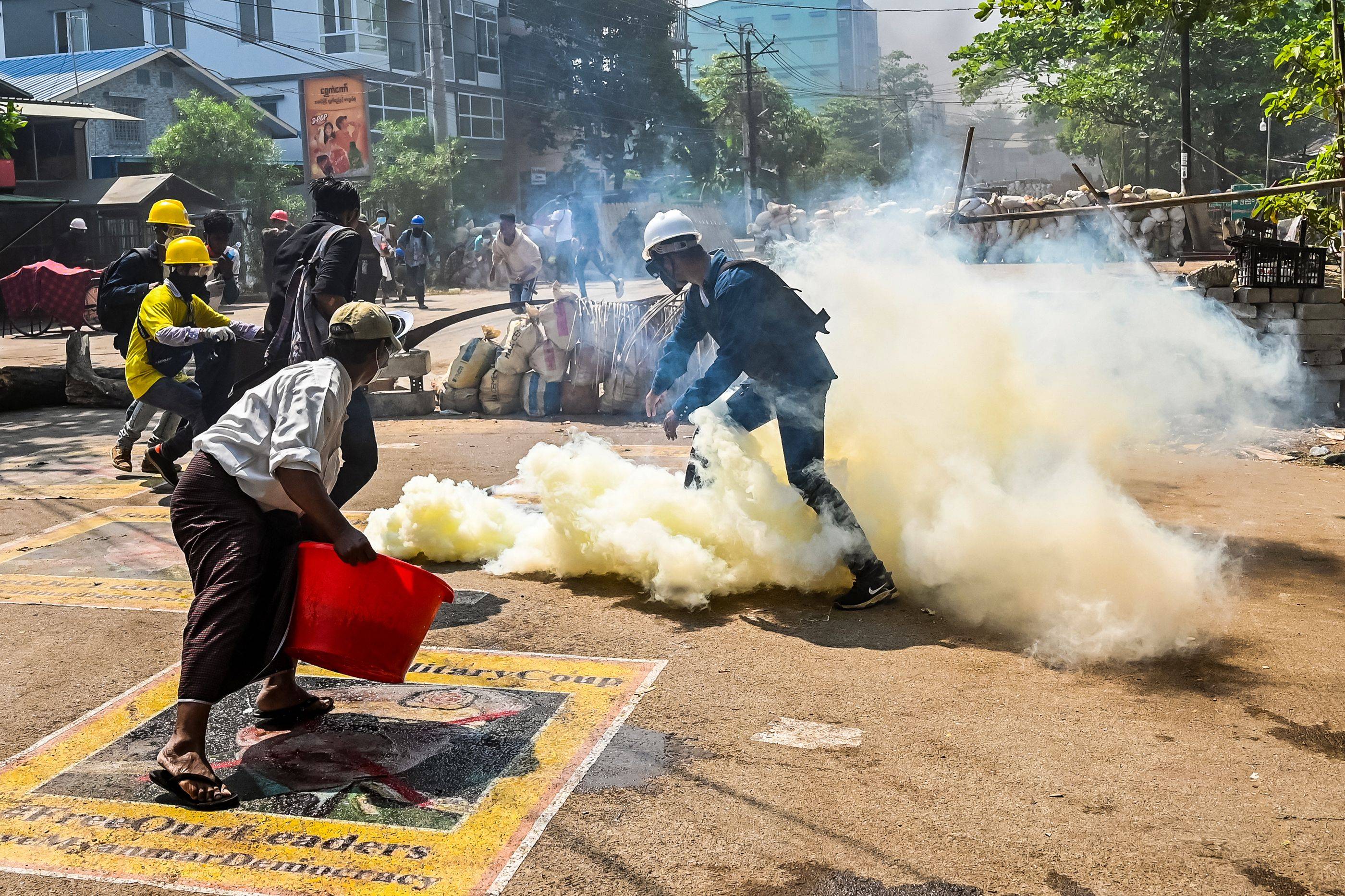 A man stands on a poster featuring armed forces chief Gen. Min Aung Hlaing as he attempts to douse tear gas during a crackdown by security forces in Yangon on Friday. | AFP-Jiji