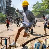 A protester jumps over a makeshift barricade during a crackdown by security forces in Yangon\'s Thaketa township on Friday. | AFP-JIJI