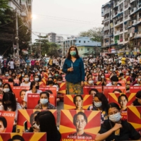 Protesters holding placards with the image of detained Myanmar civilian leader Aung San Suu Kyi sit along a street before a candlelight vigil during a demonstration against the military coup, in Yangon on March 12. | AFP-JIJI