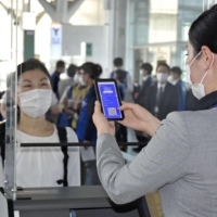 An All Nippon Airways Co. staff member (right) checks the CommonPass app indicating a traveler\'s COVID-19 status at Tokyo\'s Haneda Airport on Monday during a trial. | KYODO