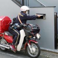A post office worker delivers a COVID-19 vaccine coupon for older people in Hachioji, Tokyo, on Wednesday. | KYODO