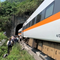 People walk next to a train that derailed in a tunnel north of Hualien, Taiwan, on Friday.  | TAIWAN\'S NATIONAL FIRE AGENCY / VIA REUTERS