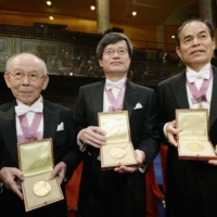 Physicist Isamu Akasaki (left), physicist Hiroshi Amano (center), a professor at the University of Nagoya, and Japan-born American Shuji Nakamura, a professor at the University of California, Santa Barbara, hold their 2014 Nobel Prizes in physics for inventing the world\'s first efficient blue light-emitting diodes in December of that year in Stockholm.  | KYODO