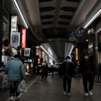 Pedestrians wearing protective masks walk through a shopping district in Kawasaki in February. | BLOOMBERG
