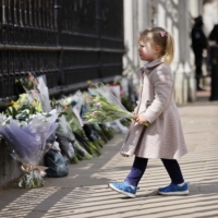 A girl adds to floral tributes against the railings at the front of Buckingham Palace in central London on Friday.  | AFP-JIJI
