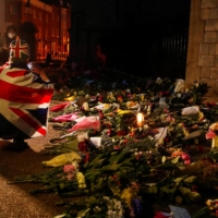A mourner draped in a British Union Jack flag takes pictures of the flowers placed outside Windsor Castle, near London, on Friday.  | REUTERS