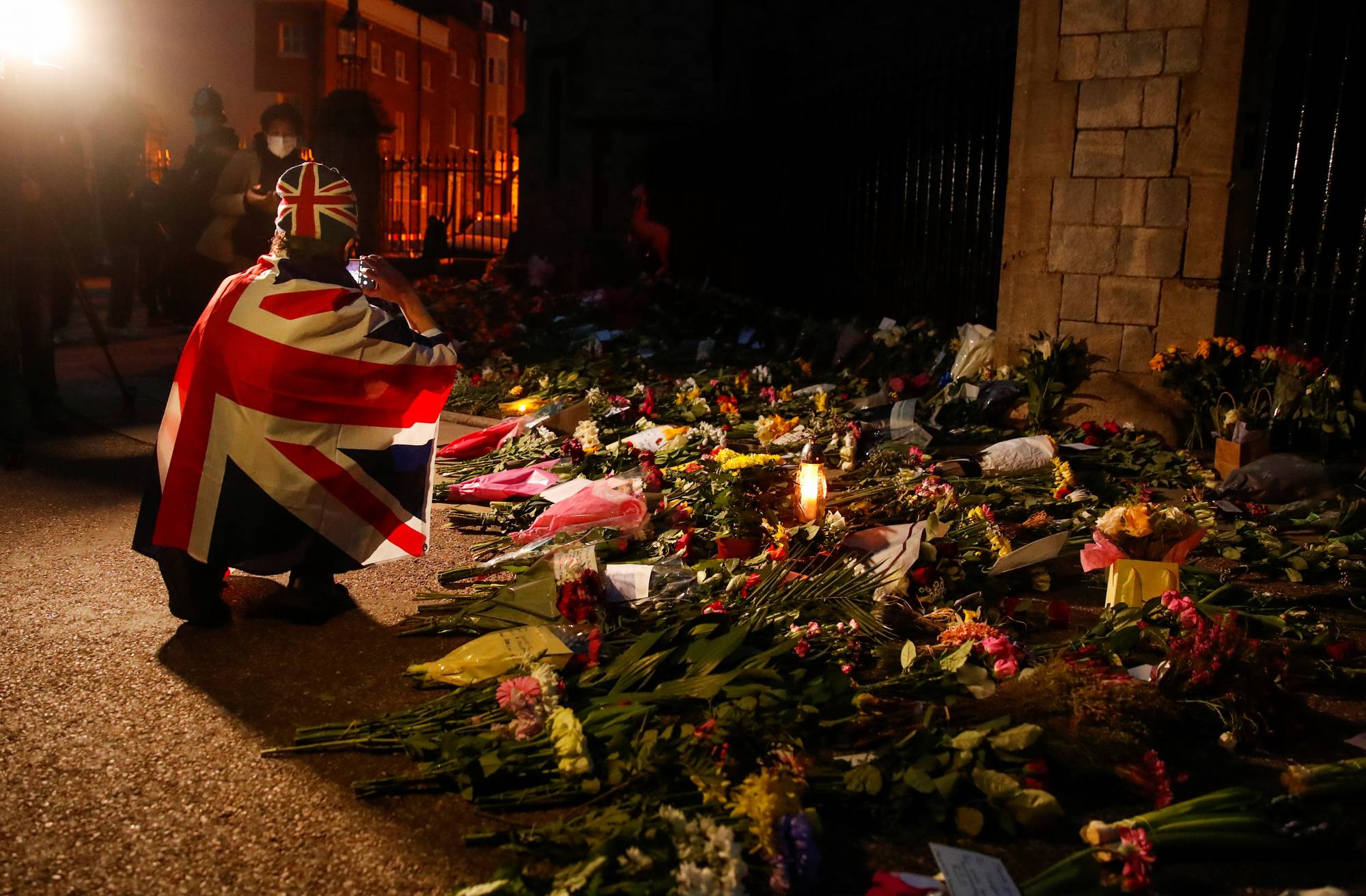 A mourner draped in a British Union Jack flag takes pictures of the flowers placed outside Windsor Castle, near London, on Friday.  | REUTERS