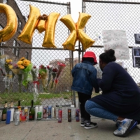 A woman and a young child light a candle at a makeshift memorial for hip-hop star DMX outside White Plains hospital in White Plains, New York, on Friday. DMX, the hardcore hip-hop star whose ominous, snarling raps chronicled the violence and struggles of the American street, died the same day. He was 50 years old.  | AFP-JIJI