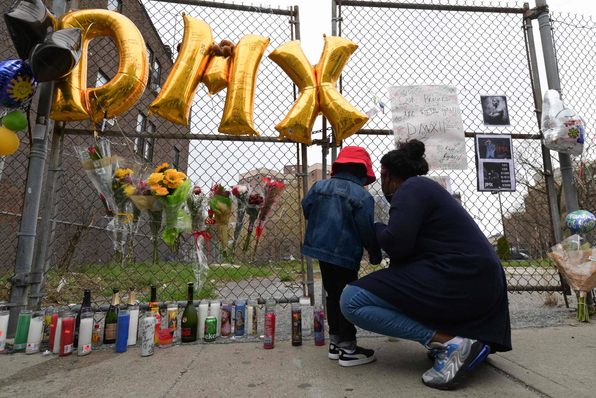 A woman and a young child light a candle at a makeshift memorial for hip-hop star DMX outside White Plains hospital in White Plains, New York, on Friday. DMX, the hardcore hip-hop star whose ominous, snarling raps chronicled the violence and struggles of the American street, died the same day. He was 50 years old. | AFP-JIJI