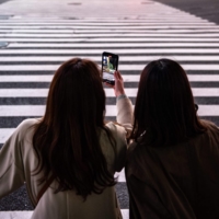 A woman films with her mobile phone on a street in Tokyo\'s Shibuya Ward on Friday. | AFP-JIJI