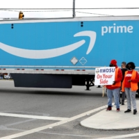 People hold a banner as members of a congressional delegation arrive to show their support for a union for workers at an Amazon facility in Bessemer, Alabama. | REUTERS