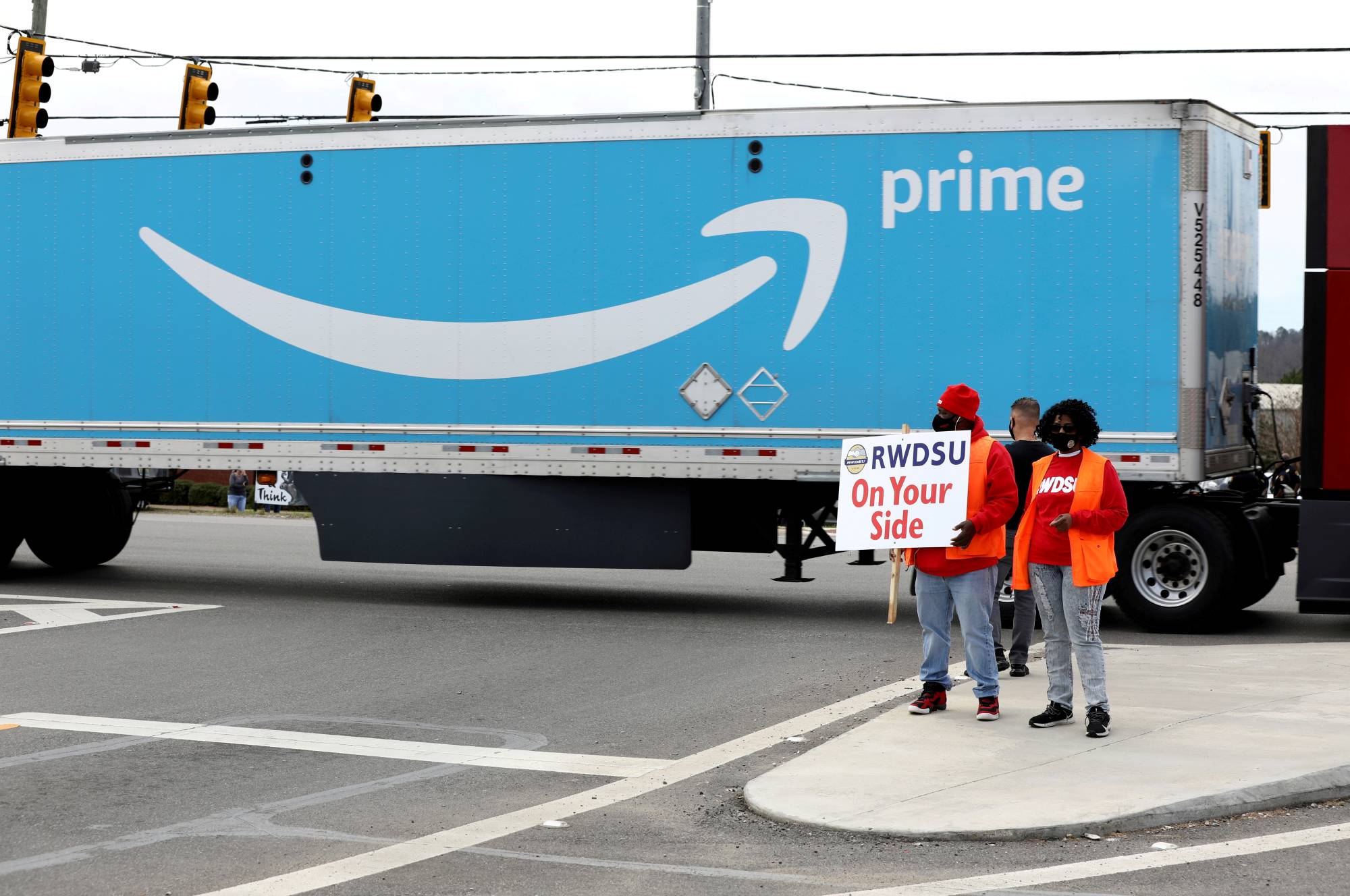 People hold a banner as members of a congressional delegation arrive to show their support for a union for workers at an Amazon facility in Bessemer, Alabama. | REUTERS