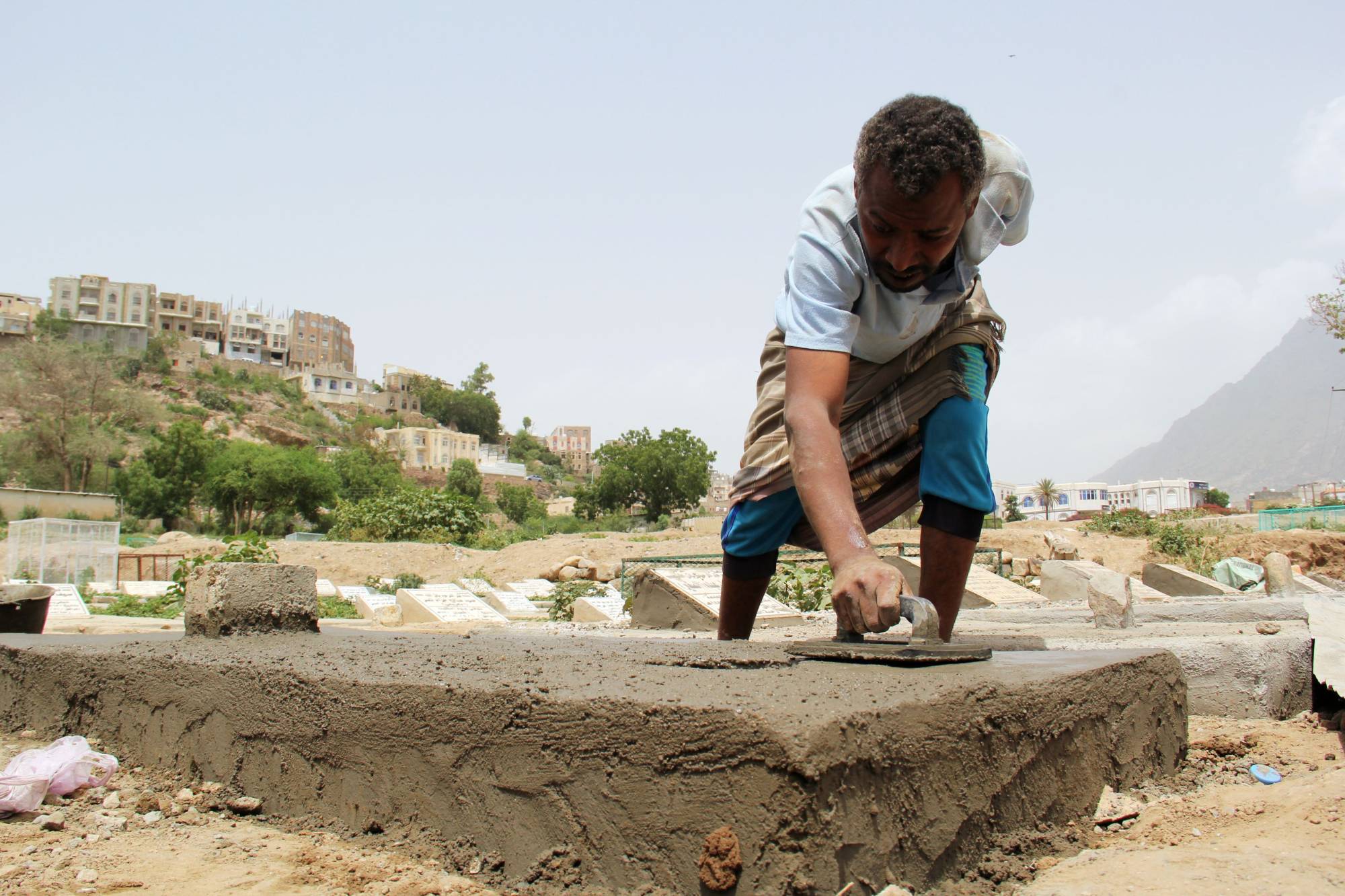 A worker builds a tombstone at a cemetery where victims of the coronavirus disease are buried in Taiz, Yemen, in June 2020.   | REUTERS 