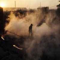 A Chinese laborer walks through steam next to a furnace and cooling pit at an unauthorized steel factory in 2016 in Inner Mongolia, China. | GETTY IMAGES / VIA BLOOMBERG