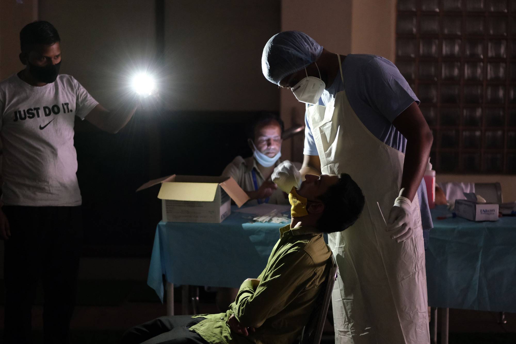 A health worker takes a swab sample during a power cut at a temporary COVID-19 testing site in New Delhi on Friday.  | BLOOMBERG 