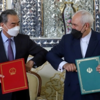 Iranian Foreign Minister Mohammad Javad Zarif and Chinese State Councilor Wang Yi bump elbows during the signing ceremony of a 25-year cooperation agreement, in Tehran on March 27.  | WEST ASIA NEWS AGENCY / VIA REUTERS 