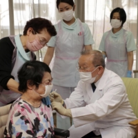 A doctor administers a COVID-19 vaccine with a help of a nurse at a care facility for older people in the city of Kyoto on April 12. | POOL / VIA KYODO