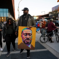 A man carries a portrait of George Floyd as people gather outside the Barclays Center in Brooklyn, New York, on Tuesday.  | MICHELLE V. AGINS / THE NEW YORK TIMES