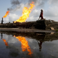 A woman walks near gas furnaces at a flow station in Ughelli, Delta state, Nigeria, in September 2020. | REUTERS