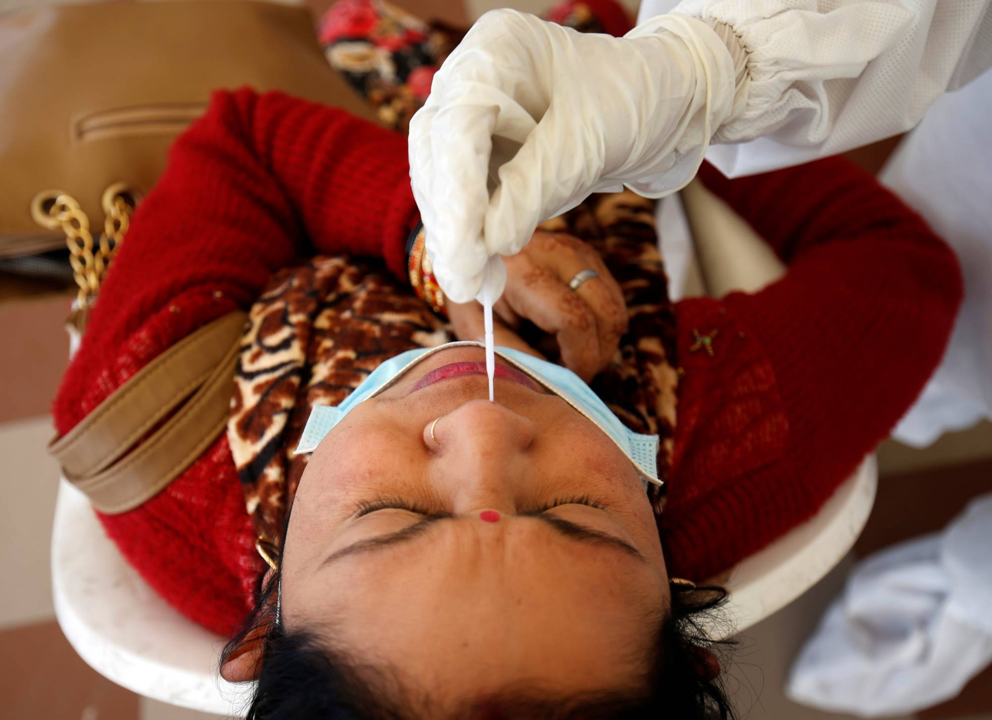 A health care worker collects a swab sample from a woman during a rapid antigen testing campaign for the coronavirus in Ahmedabad, India, in December 2020. | REUTERS