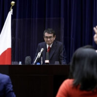 A viral gamble: Taro Kono, Japan\'s regulatory reform and vaccine minister, listens to a question from a journalist from behind a transparent screen during a news conference in February. Kono has pointed out that traveling during third and fourth waves of the pandemic may be riskier than waiting for your shot in Japan. | BLOOMBERG