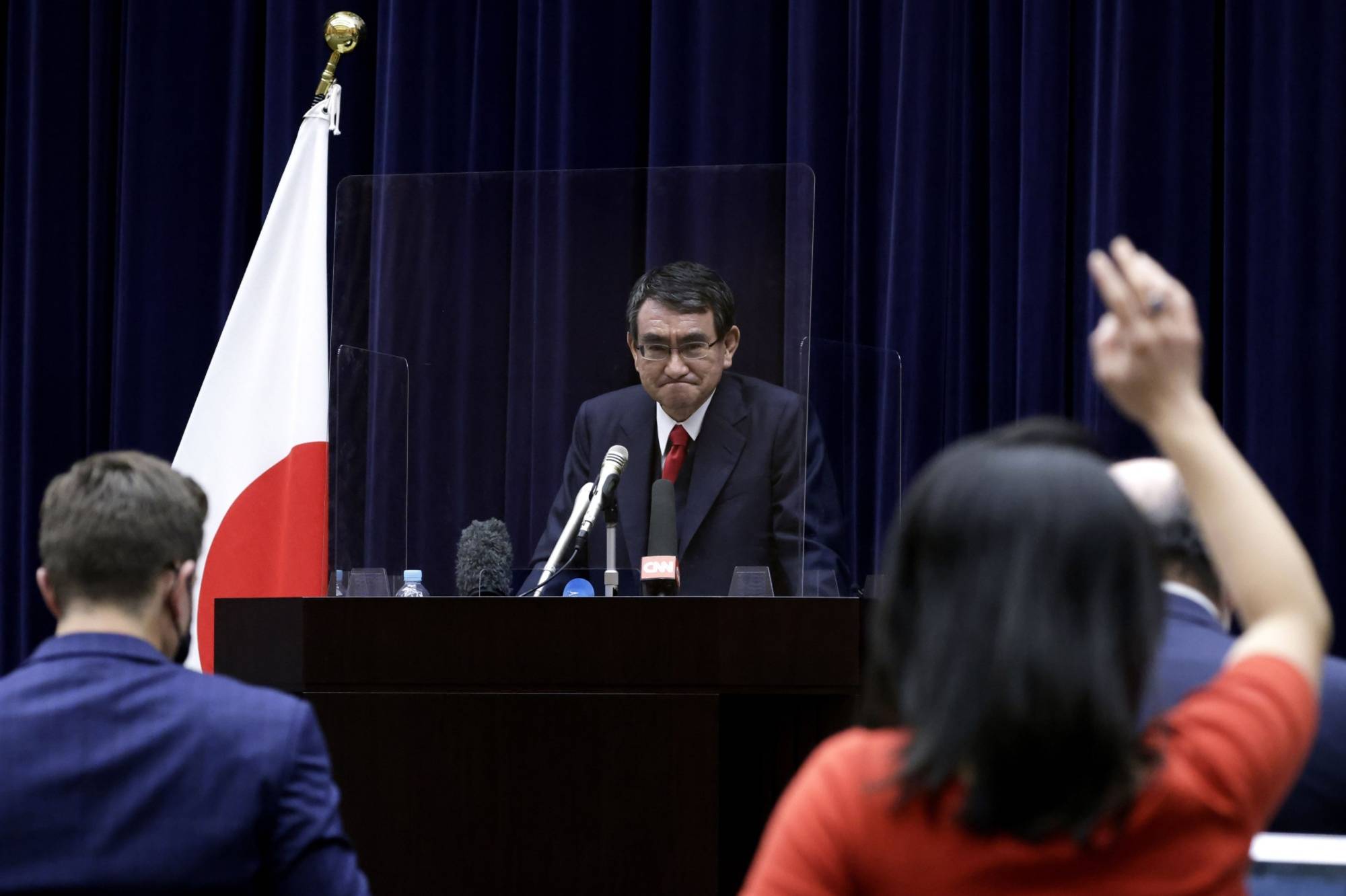 A viral gamble: Taro Kono, Japan's regulatory reform and vaccine minister, listens to a question from a journalist from behind a transparent screen during a news conference in February. Kono has pointed out that traveling during third and fourth waves of the pandemic may be riskier than waiting for your shot in Japan. | BLOOMBERG