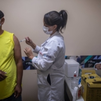 In process: A health care worker administers a dose of the Sinovac Biotech CoronaVac COVID-19 vaccine to a person at a community shelter in Sao Paulo, Brazil, on April 22. The Brazilian government is adding 1.6 billion reals ($286 million) in funding to purchase vaccines, medicines and expand intensive care centers around the country.  | BLOOMBERG