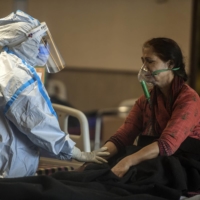 A health care worker speaks to a COVID-19 patient at a temporary treatment site set up near a hospital in Delhi on Friday.  | ATUL LOKE / THE NEW YORK TIMES