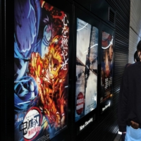 Movie goers line up next to an advertisement for \"Demon Slayer: Kimetsu no Yaiba the Movie: Mugen Train\" outside a cinema in Tokyo in October. | BLOOMBERG
