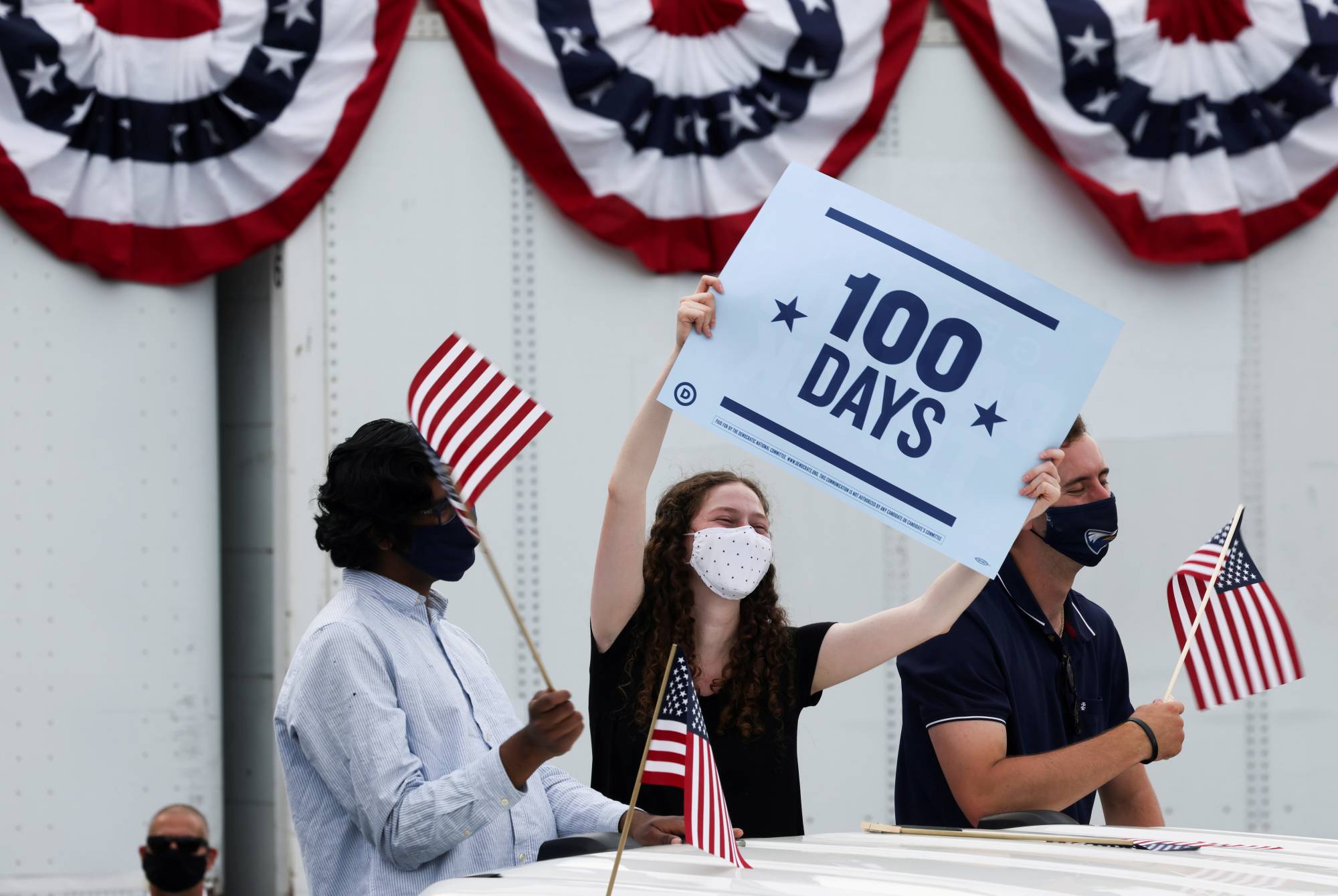 People hold flags and a sign as they attend a Democratic National Committee drive-in rally to celebrate U.S. President Joe Biden's 100th day in office, in Duluth, Georgia, on Thursday. | REUTERS