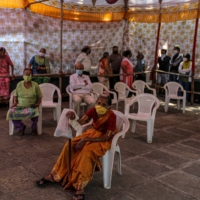 People wait at a COVID-19 vaccination center set up at a municipal hospital in Pune, India, on Wednesday. As infections surge by more than 300,000 cases for 14 straight days, pushing India’s tally past 20 million, the country’s limited ability to track new mutations emerging from its outbreak is a growing concern for scientists. | BLOOMBERG