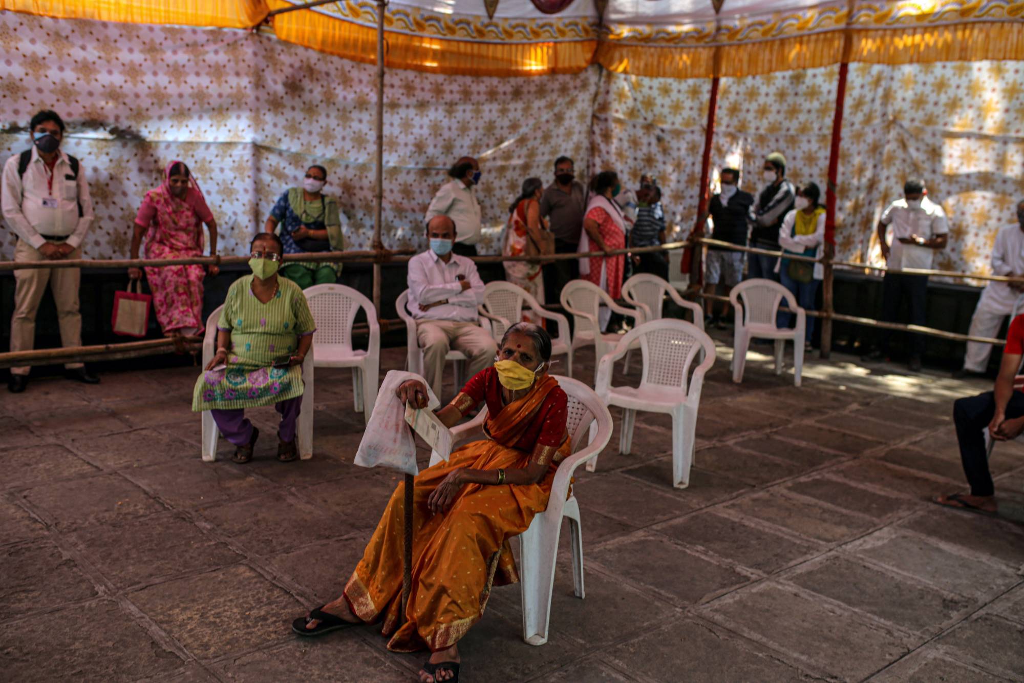 People wait at a COVID-19 vaccination center set up at a municipal hospital in Pune, India, on Wednesday. As infections surge by more than 300,000 cases for 14 straight days, pushing India’s tally past 20 million, the country’s limited ability to track new mutations emerging from its outbreak is a growing concern for scientists. | Bloomberg